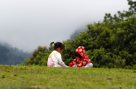 Asian little child girl helped to put shoes on the sister on the grass at Ang Khang mountain, Fang Chiang Mai. Tourist attraction in northern of Thailand.