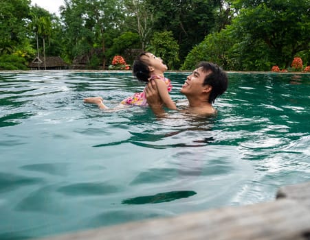 Portrait of Father and daughter enjoying a summer holiday in swimming pool at Northern resort of Thailand.