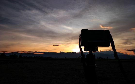 Digital camera back side over tripod on high mountains with sunset sky background.