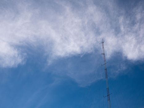 TV and radio pole telecommunication antenna on clouds and blue sky background.