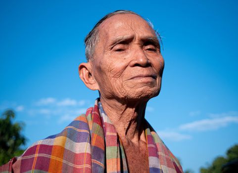 Senior Asian man with a loincloth covering his shoulders, standing over the bright sky background.