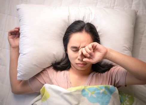 Asian young woman is sleepy while alarm clock on bed in the morning.