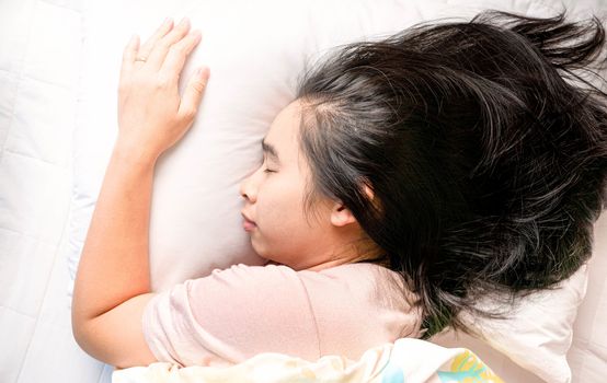 Top view of attractive Asian young woman sleeping well in bed hugging soft white pillow. Health care concept.