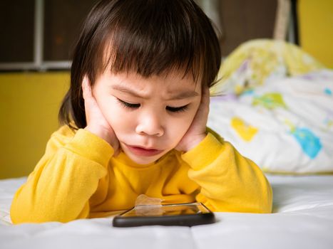 Asian little girl watching smartphone on their bed. Kid addicted to mobile phones.