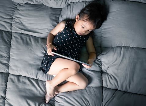 Asian little girl watching laptop on their bed. Kid addicted to mobile phones.