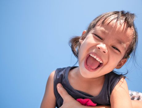 Adorable Asian child girl having fun in spring, smiling and looking at camera of bright sky background.