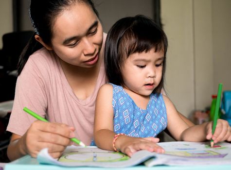 Asian mother helping daughter doing homework after school. Home teaching concept.