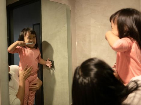 Adorable Asian child girl brushing your teeth in front of a mirror with mother in the morning. Health care concept.