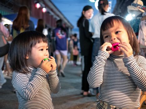 Lampang, Thailand; 5 October 2019 - Adorable Asian child girl with her sister having fun with Dracula teeth plastic toys in Kad Kong Ta Walking Street.