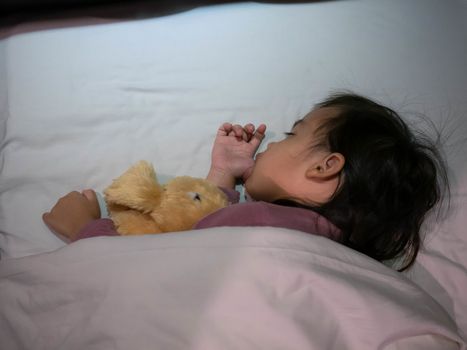 Top view of Adorable Asian child girl sleeping well in bed hugging doll and sucking her thumb. Health care concept.