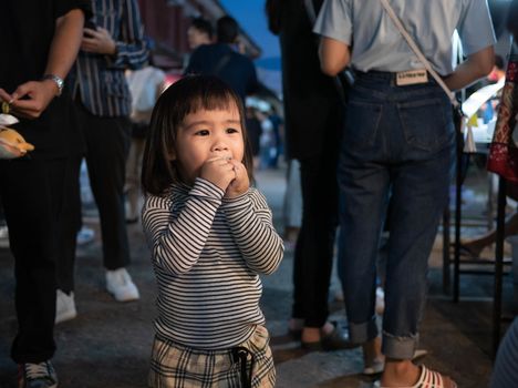 Lampang, Thailand; 5 October 2019 - Adorable Asian child girl having fun with Dracula teeth plastic toys in Kad Kong Ta Walking Street.