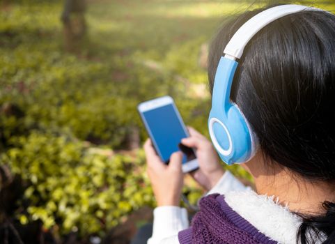 Asian young girl listening to music by headphone in the garden. Technology and relaxation concept.