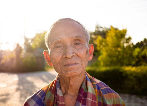 Senior Asian man with a loincloth covering his shoulders, standing over the bright sky background.