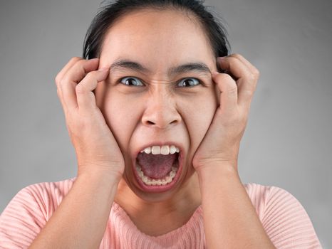 Furious and frustrated woman yelling with hand on face, Isolated on grey background. Emotional and expression concept.