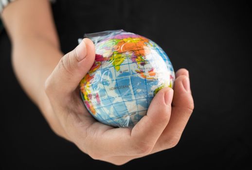 Woman hand holds the earth in plastic bag on black background. Global warming due to pollution by plastic debris. The concept of Earth Day.