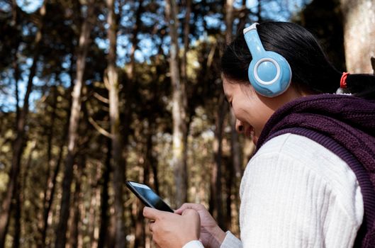 Asian young girl listening to music by headphone in the garden. Technology and relaxation concept.