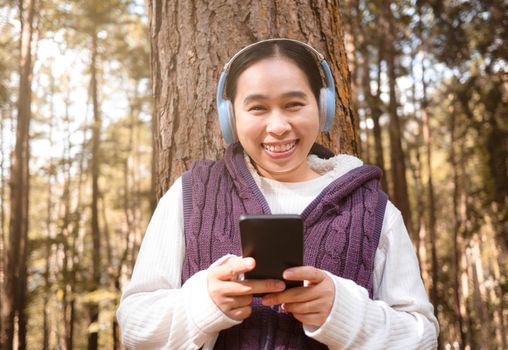 Asian young woman listening to music by headphone in the garden. Technology and relaxation concept.