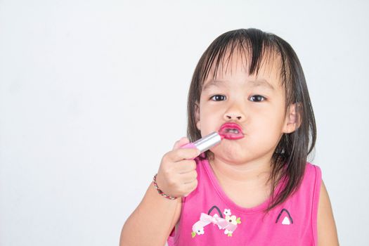 Happy Asian child girl with apply red lipstick wearing pink dress isolated on white background.