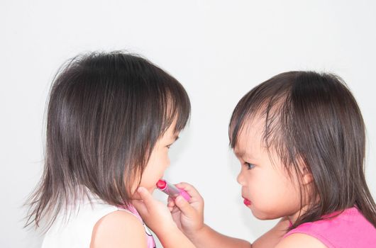 Asian child girl apply red lipstick on lips for sister on white background.