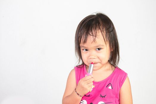 Happy Asian child girl with apply red lipstick wearing pink dress isolated on white background.