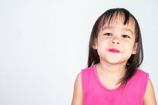 Happy Asian child girl with apply red lipstick wearing pink dress isolated on white background.