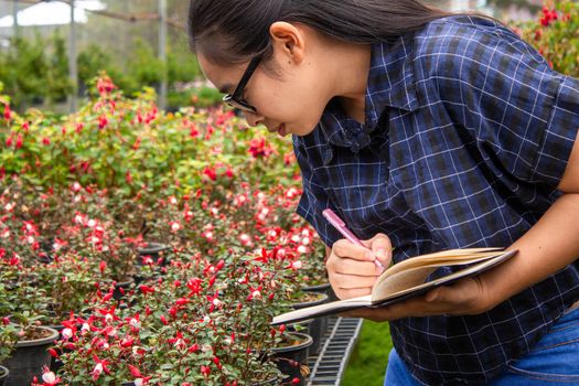 Portrait of Gardener Asian woman at work in greenhouse with notebook examines the growing flowers on the farm and diseases in greenhouse.