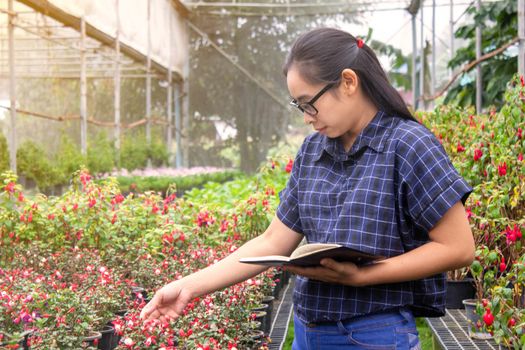Portrait of Gardener Asian woman at work in greenhouse with notebook examines the growing flowers on the farm and diseases in greenhouse.