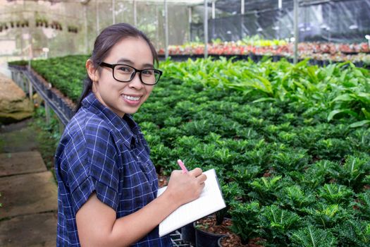 Portrait of a farmer Asian woman at work in greenhouse with notebook examines the growing seedlings on the farm and diseases in greenhouse.