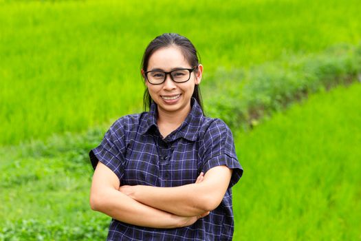 Asian farmer woman smile and cross one's arms with a look of proud on rice field background.