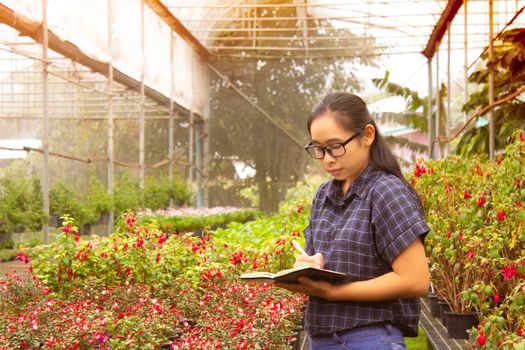 Portrait of Gardener Asian woman at work in greenhouse with notebook examines the growing flowers on the farm and diseases in greenhouse.