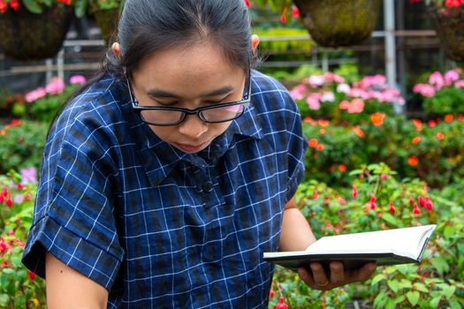 Portrait of Gardener Asian woman at work in greenhouse with notebook examines the growing flowers on the farm and diseases in greenhouse.
