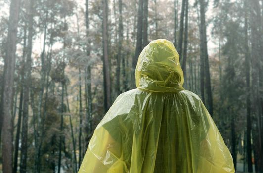 Rear of Asian woman wearing yellow raincoat stand in rain.