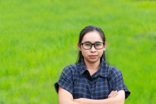 Asian farmer woman smile and cross one's arms with a look of proud on rice field background.