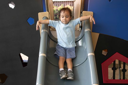 Asian little child girl having fun on slide at playground.