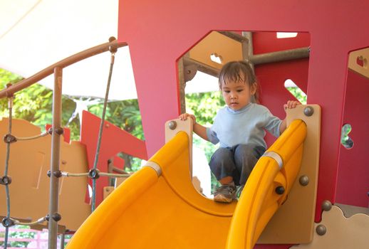 Asian little child girl having fun on slide at playground.