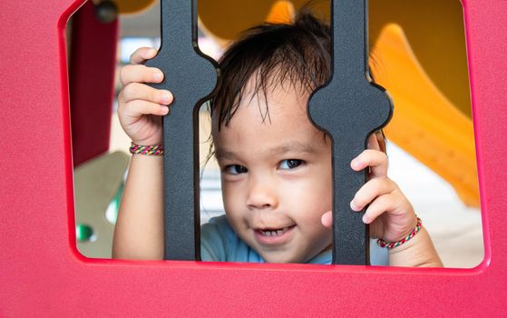 Asian little child playing peekaboo in window of small plastic house in the playground.