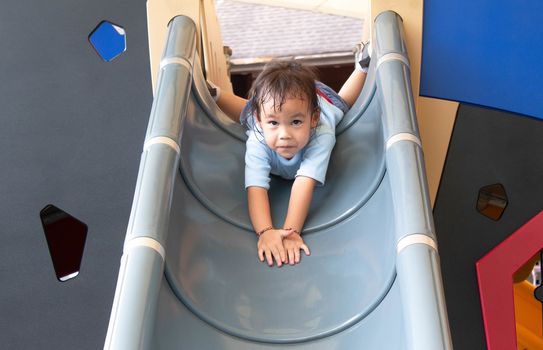 Asian little child girl having fun on slide at playground.