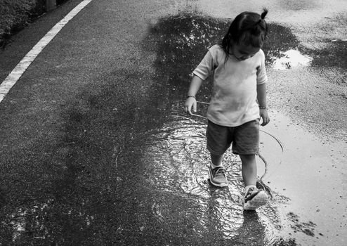 Asian little child walking through in puddle on the street.