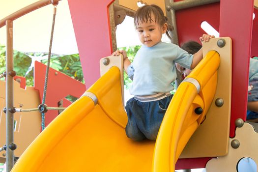 Asian little child girl having fun on slide at playground.