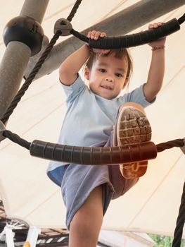 Asian little child girl having fun to climbing rope at playground in summer time.