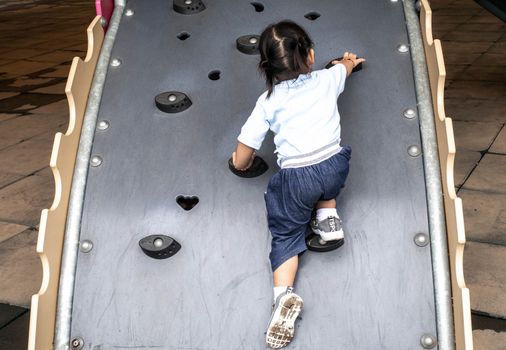 Rear of Asian little child girl climbing to slide at playground.