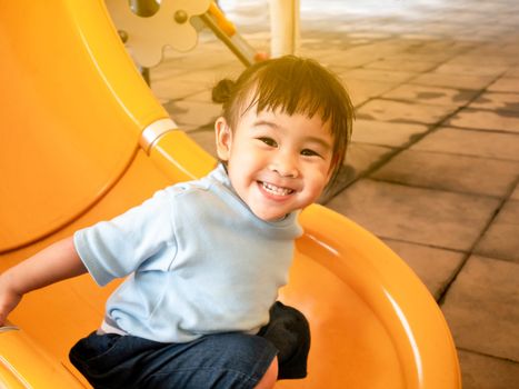 Happy Asian little child girl having fun on slide at playground.