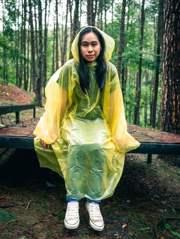 Happy Asian woman wearing yellow raincoat sitting on wooden stage in rain.