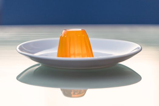 Close-up of an orange gelatin on a white plate reflected on a glass table