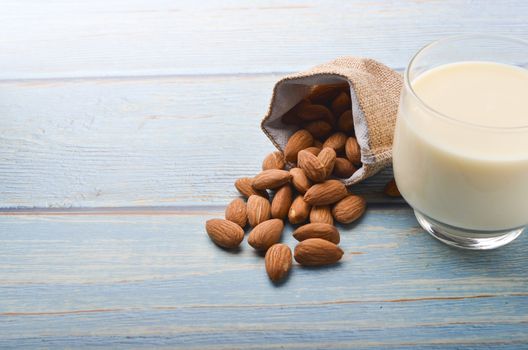 Close up view of healthy almond milk in drinking glass with seed in bowl on wooden background. Selective focus.