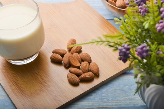 Close up view of healthy almond milk in drinking glass with seed in bowl on wooden background. Selective focus.