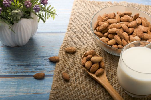 Close up view of healthy almond milk in drinking glass with seed in bowl on wooden background. Selective focus.