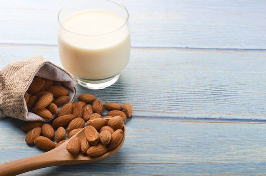 Close up view of healthy almond milk in drinking glass with seed in bowl on wooden background. Selective focus.