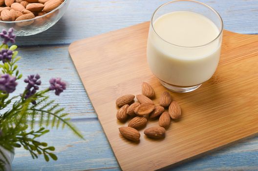 Close up view of healthy almond milk in drinking glass with seed in bowl on wooden background. Selective focus.