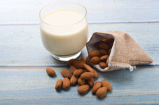 Close up view of healthy almond milk in drinking glass with seed in bowl on wooden background. Selective focus.